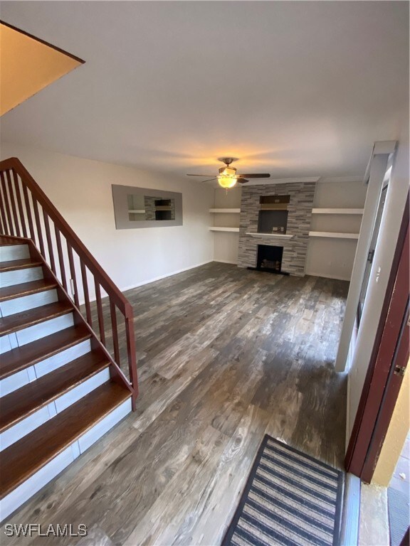 staircase with a stone fireplace, ceiling fan, and hardwood / wood-style floors