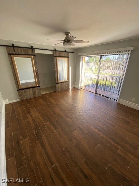 unfurnished room featuring a barn door, ceiling fan, and dark wood-type flooring