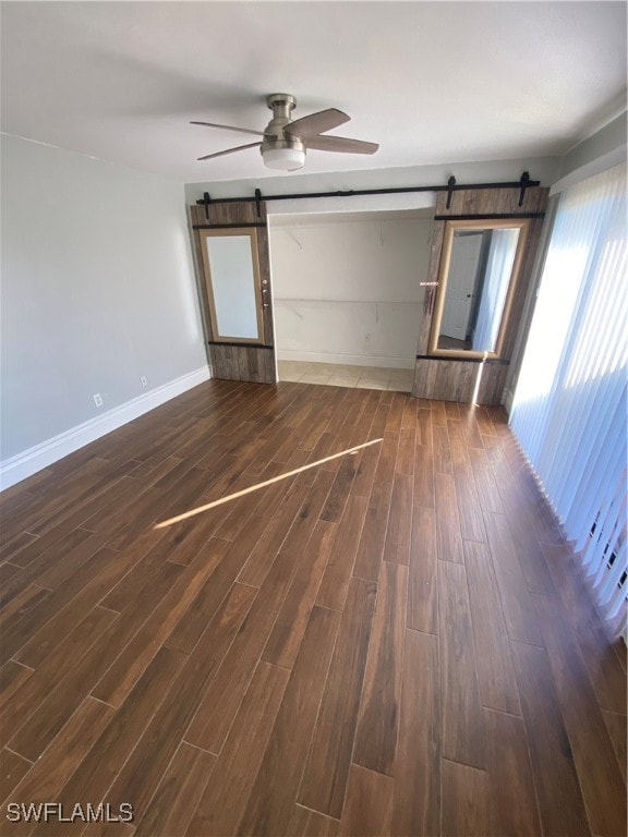 empty room with a barn door, dark hardwood / wood-style floors, and ceiling fan