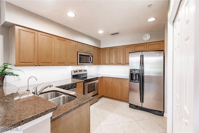 kitchen with dark stone counters, sink, light tile patterned floors, appliances with stainless steel finishes, and kitchen peninsula