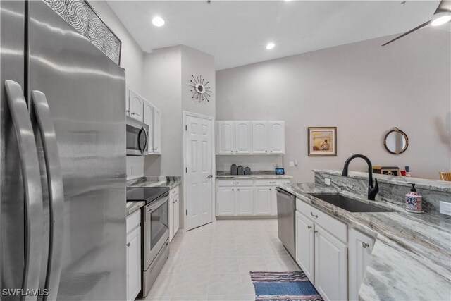 kitchen with light tile patterned floors, light stone counters, stainless steel appliances, a sink, and white cabinets