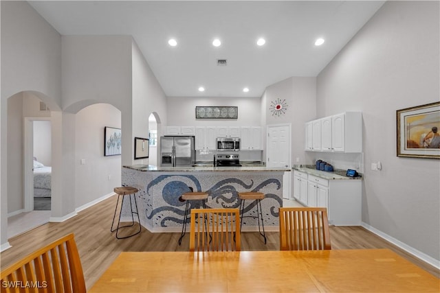 kitchen featuring white cabinets, a towering ceiling, light wood-style flooring, appliances with stainless steel finishes, and a breakfast bar