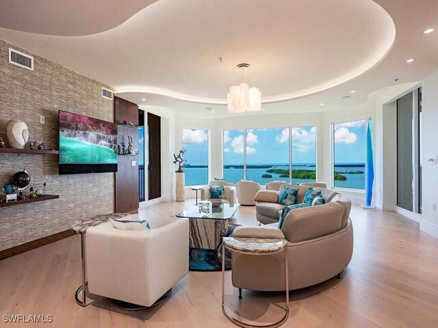 living room featuring a chandelier, a tray ceiling, and light hardwood / wood-style flooring