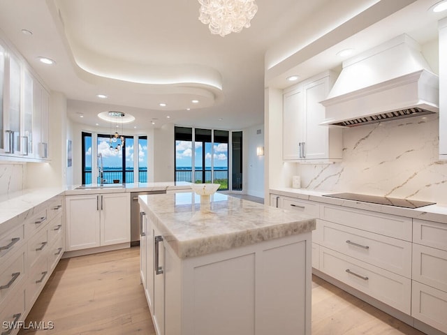 kitchen with premium range hood, black electric cooktop, light hardwood / wood-style floors, white cabinetry, and a chandelier