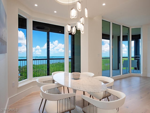 dining area with light wood-type flooring, a water view, and a healthy amount of sunlight