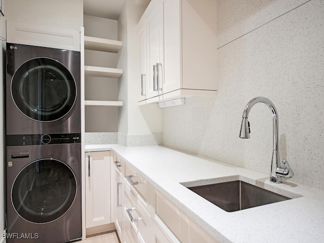 clothes washing area with stacked washer / drying machine, cabinets, and sink