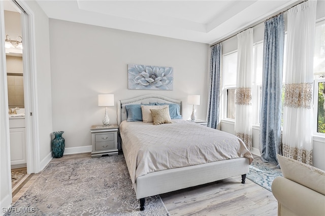 bedroom featuring light wood-type flooring, a tray ceiling, and connected bathroom