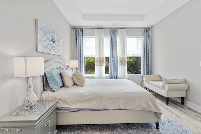 bedroom with a tray ceiling and light hardwood / wood-style flooring