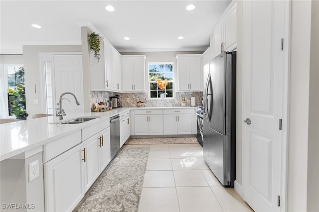 kitchen with ornamental molding, stainless steel appliances, sink, white cabinets, and light tile patterned flooring