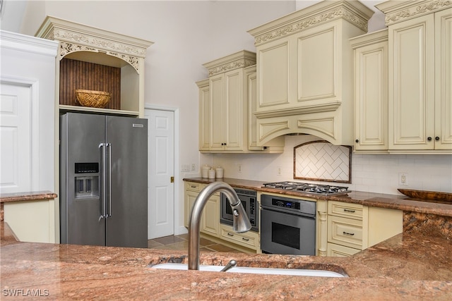 kitchen with backsplash, cream cabinets, sink, appliances with stainless steel finishes, and stone countertops