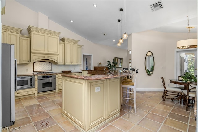 kitchen with appliances with stainless steel finishes, tasteful backsplash, pendant lighting, cream cabinetry, and an island with sink