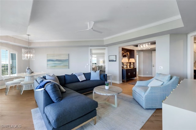 living room featuring a raised ceiling, ceiling fan with notable chandelier, light hardwood / wood-style flooring, and crown molding