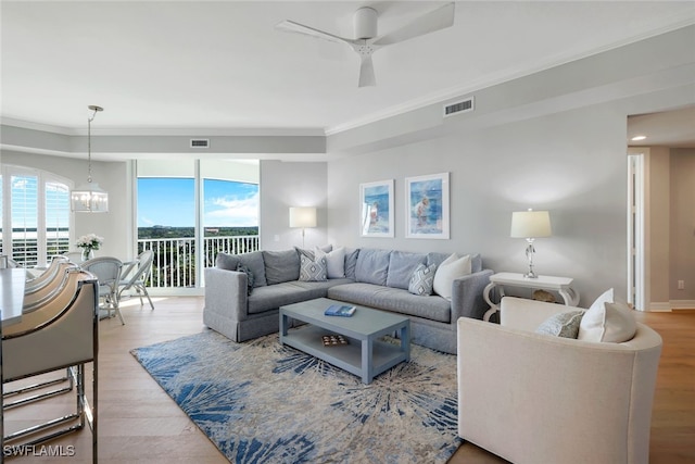 living room with crown molding, light hardwood / wood-style floors, and ceiling fan with notable chandelier