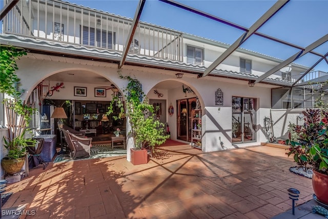 back of property featuring glass enclosure, a balcony, and a patio