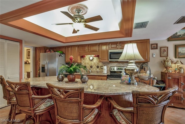 kitchen with a kitchen bar, light tile patterned floors, stainless steel appliances, and a raised ceiling