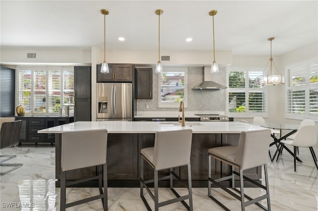 kitchen featuring a breakfast bar, backsplash, a kitchen island with sink, wall chimney exhaust hood, and stainless steel appliances