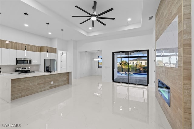 kitchen with ceiling fan, hanging light fixtures, a raised ceiling, white cabinets, and appliances with stainless steel finishes