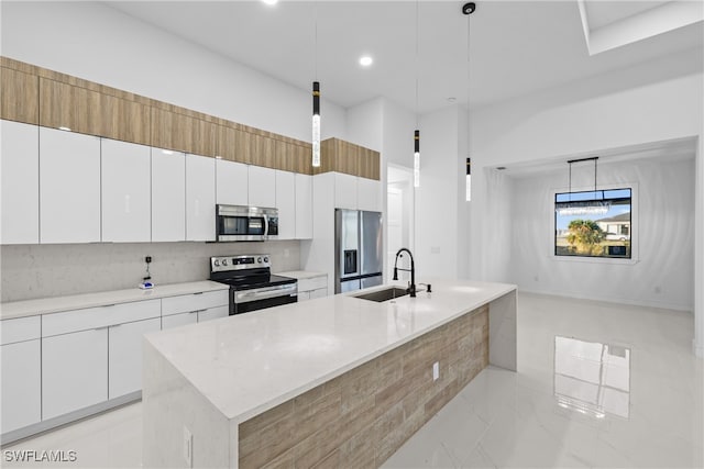 kitchen with a center island with sink, sink, hanging light fixtures, white cabinetry, and stainless steel appliances