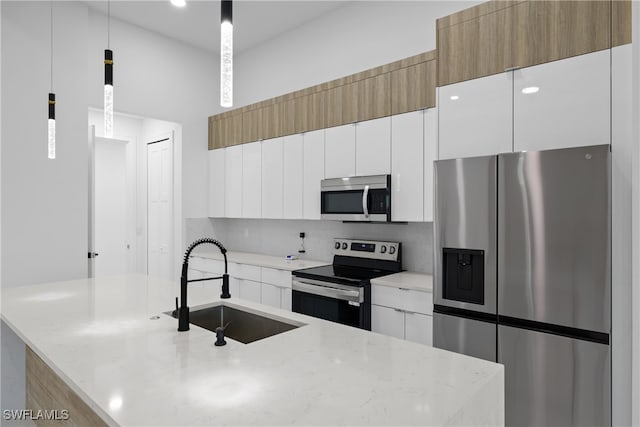 kitchen with light stone countertops, appliances with stainless steel finishes, sink, white cabinetry, and hanging light fixtures