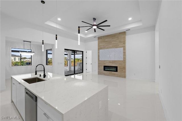 kitchen with stainless steel dishwasher, sink, white cabinets, hanging light fixtures, and an island with sink