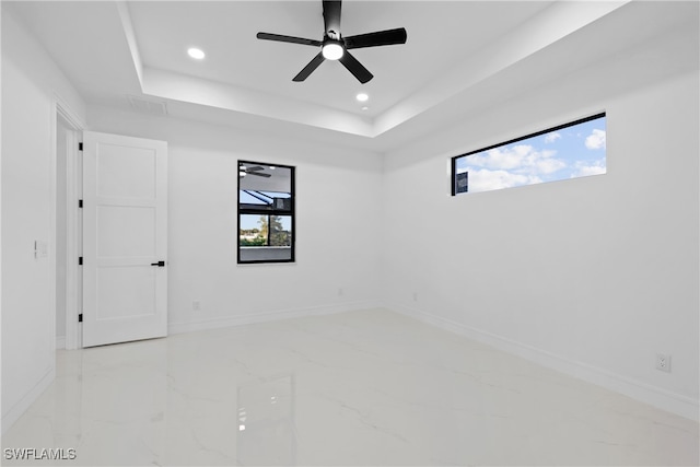 empty room with a raised ceiling, ceiling fan, and plenty of natural light