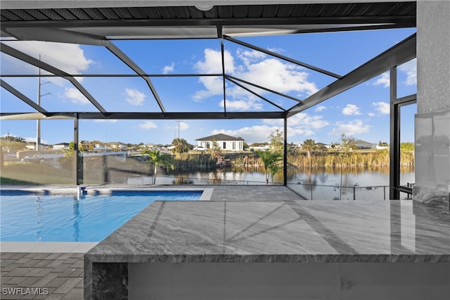 view of pool featuring glass enclosure, a water view, and a patio