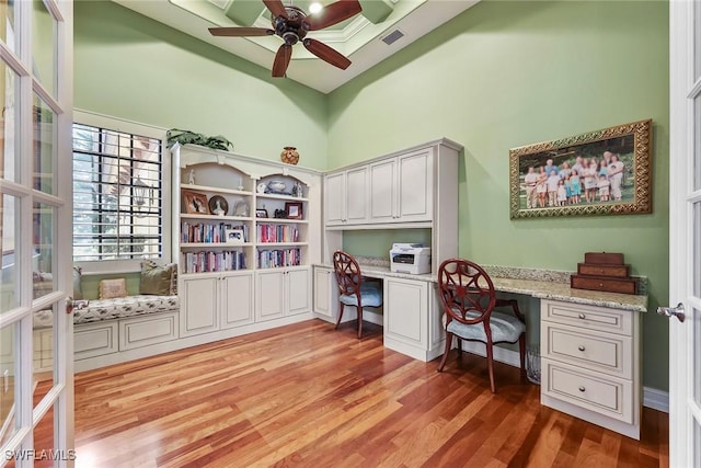 office area with ceiling fan, built in desk, a high ceiling, and light hardwood / wood-style flooring