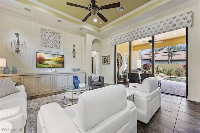 living room featuring a tray ceiling, dark tile patterned flooring, ceiling fan, and ornamental molding