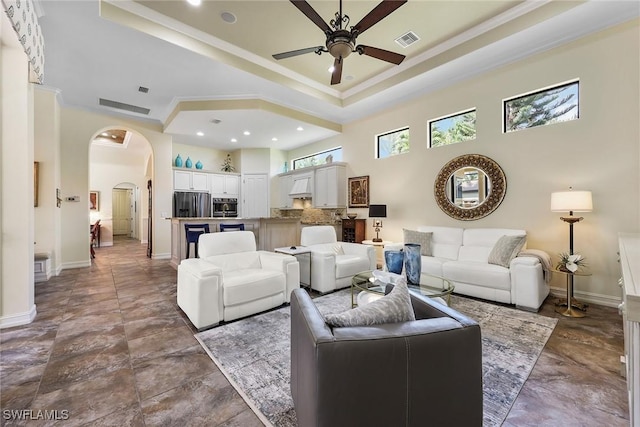 living room with a towering ceiling, a tray ceiling, ceiling fan, and crown molding