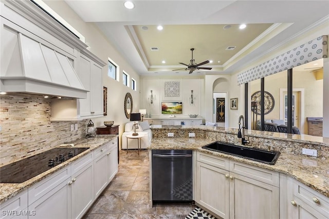 kitchen with sink, light stone countertops, black electric cooktop, a tray ceiling, and custom range hood