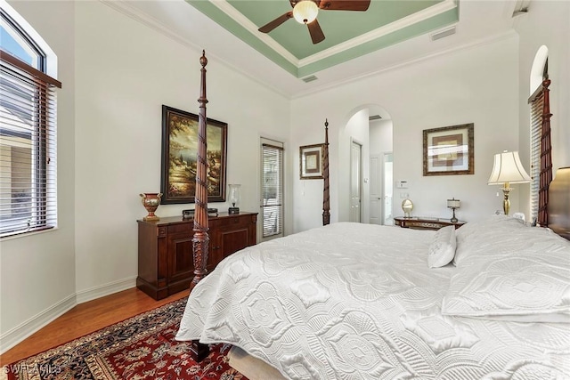 bedroom featuring wood-type flooring, a raised ceiling, ceiling fan, and crown molding