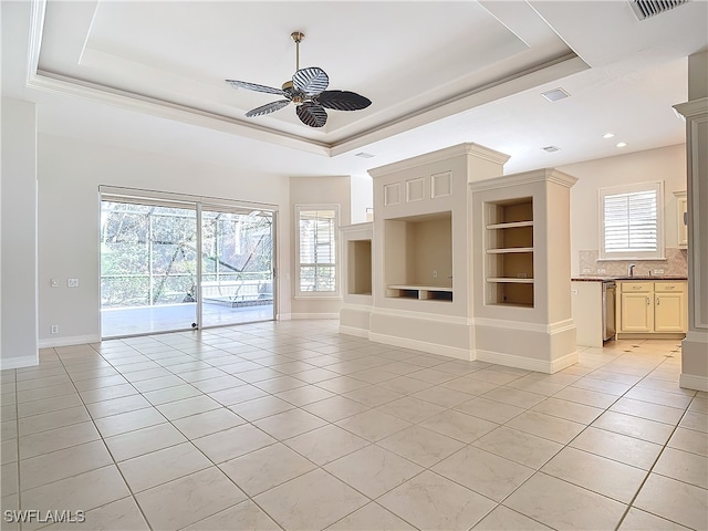 unfurnished living room featuring a tray ceiling, ceiling fan, built in features, and light tile patterned flooring