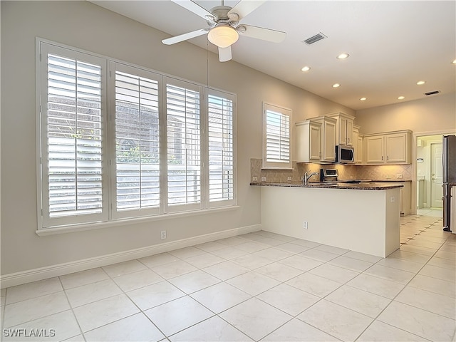 kitchen featuring dark stone counters, range, decorative backsplash, light tile patterned floors, and kitchen peninsula