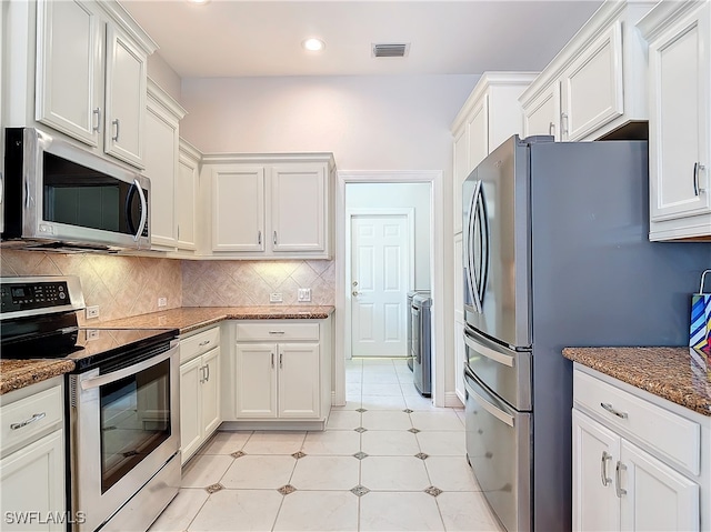 kitchen featuring white cabinets, decorative backsplash, dark stone countertops, washing machine and dryer, and stainless steel appliances