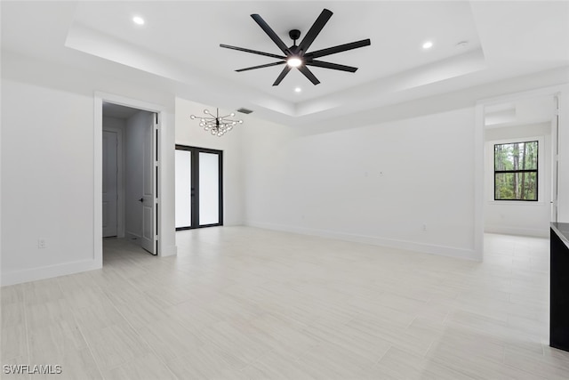 empty room featuring a raised ceiling and ceiling fan with notable chandelier