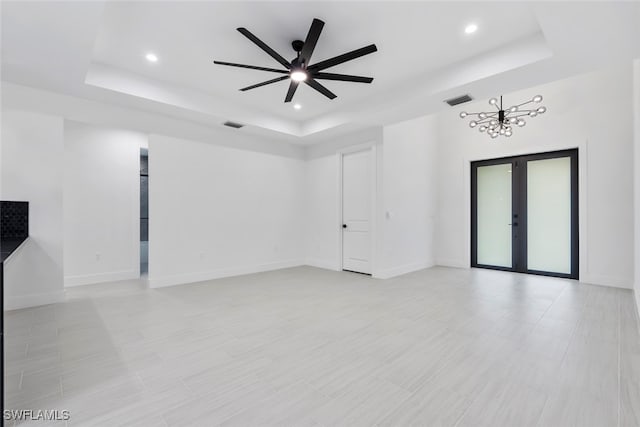 unfurnished room with ceiling fan with notable chandelier, french doors, and a tray ceiling