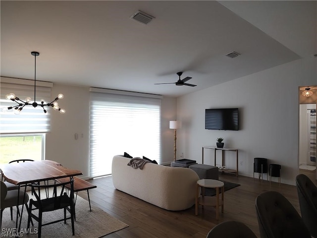 living room with ceiling fan with notable chandelier, a healthy amount of sunlight, lofted ceiling, and dark wood-type flooring