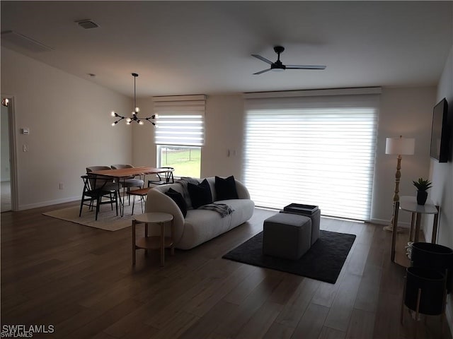 living room featuring ceiling fan with notable chandelier and dark wood-type flooring