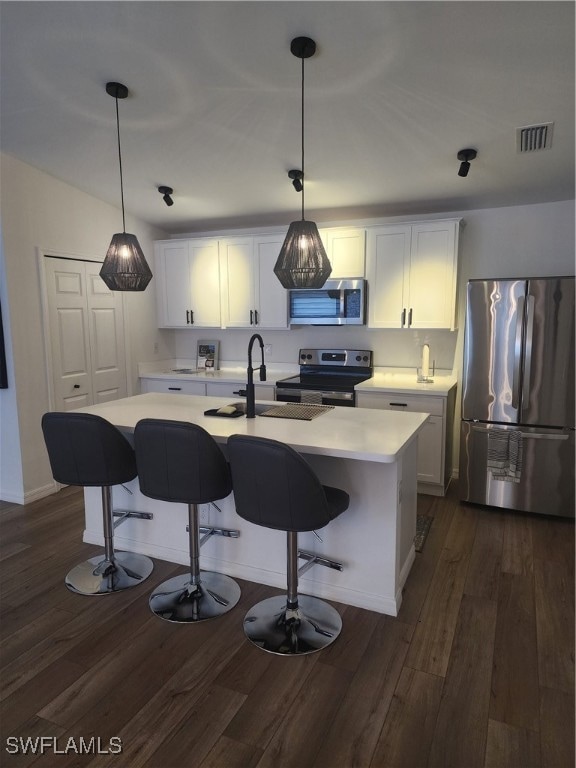 kitchen featuring white cabinetry, dark wood-type flooring, an island with sink, decorative light fixtures, and appliances with stainless steel finishes