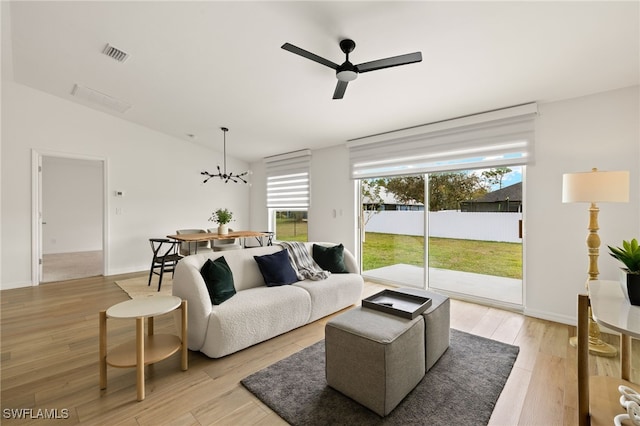 living area featuring ceiling fan with notable chandelier, visible vents, baseboards, vaulted ceiling, and light wood-style floors