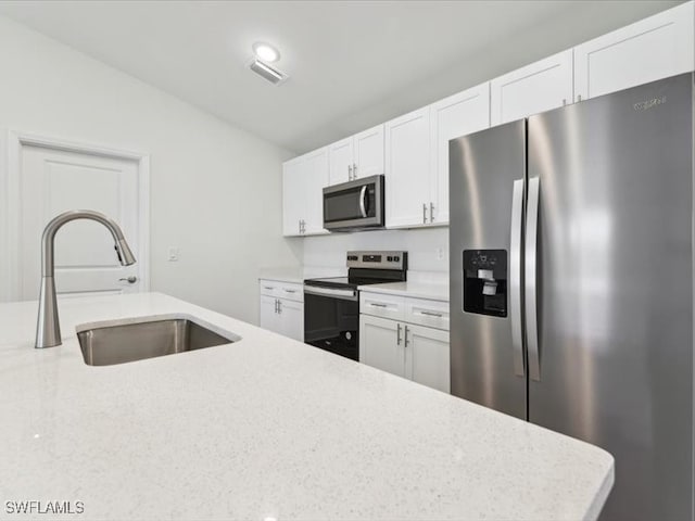 kitchen featuring appliances with stainless steel finishes, light stone counters, white cabinetry, and sink