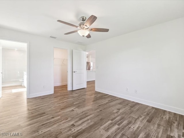 unfurnished bedroom featuring ensuite bath, ceiling fan, a walk in closet, a closet, and hardwood / wood-style flooring