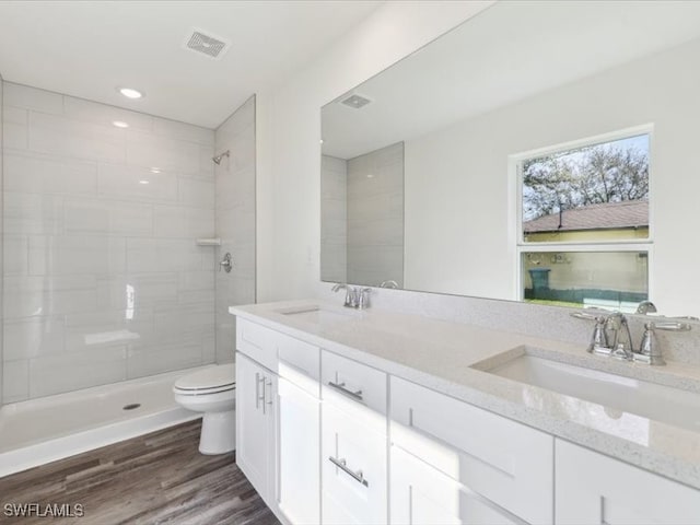 bathroom with a tile shower, vanity, wood-type flooring, and toilet