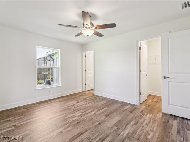 unfurnished bedroom featuring a closet, a walk in closet, light hardwood / wood-style floors, and ceiling fan