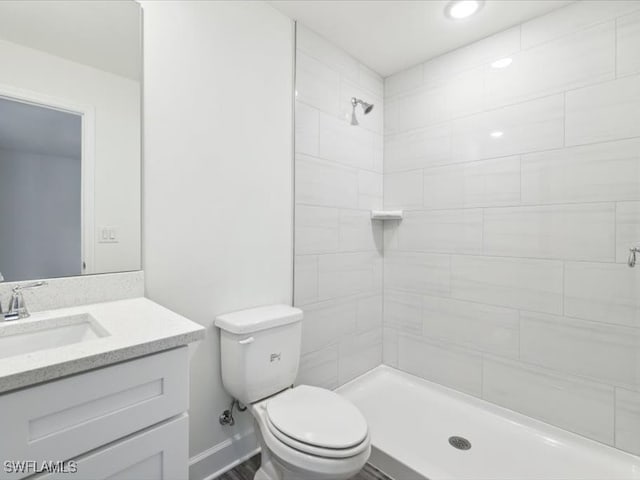 bathroom featuring a tile shower, vanity, and toilet