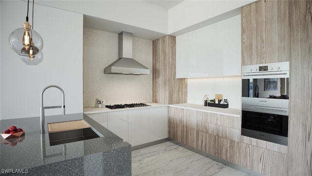 kitchen with wall chimney range hood, sink, hanging light fixtures, dark stone countertops, and stainless steel appliances