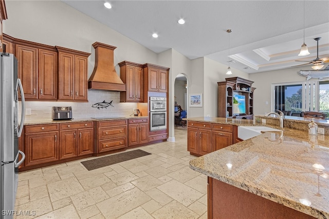 kitchen featuring sink, light stone counters, pendant lighting, custom exhaust hood, and appliances with stainless steel finishes