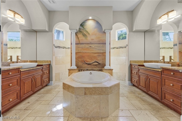 bathroom with decorative columns, tiled bath, plenty of natural light, and vanity