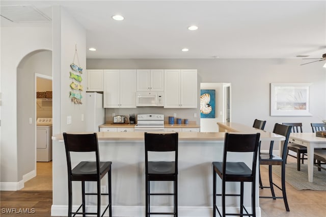 kitchen featuring a kitchen bar, white cabinets, white appliances, and washer / dryer