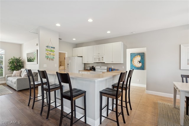 kitchen with a kitchen bar, white cabinetry, light hardwood / wood-style floors, and white appliances